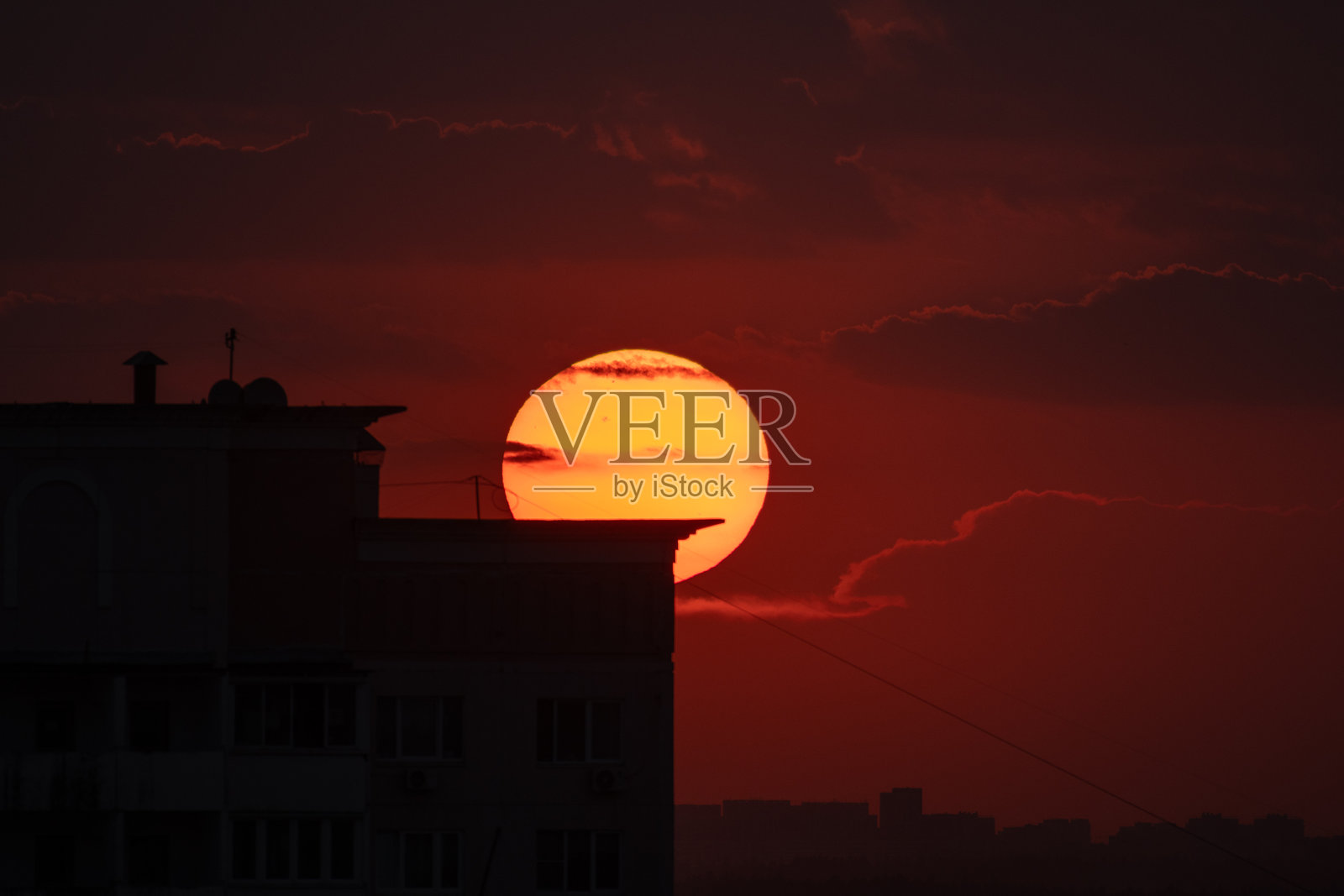 黄昏时分，巨大的太阳在建筑轮廓后落下。照片摄影图片