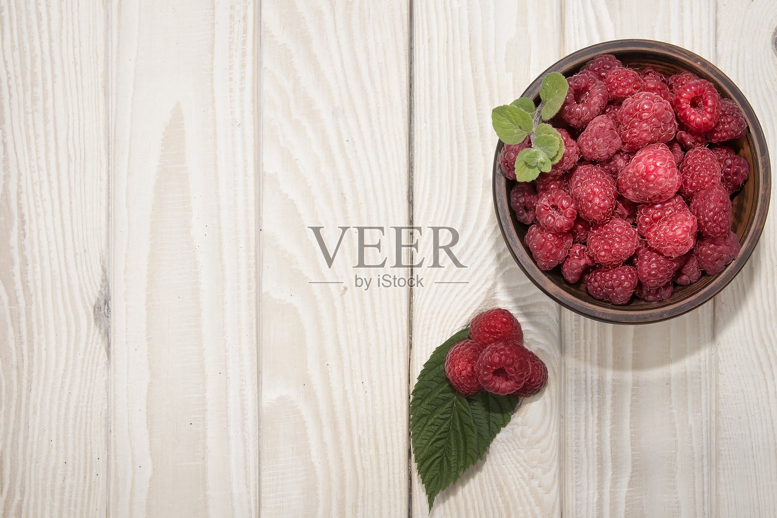 新鲜成熟的覆盆子放在陶土碗中，背景为白色木纹，俯视图照片摄影图片