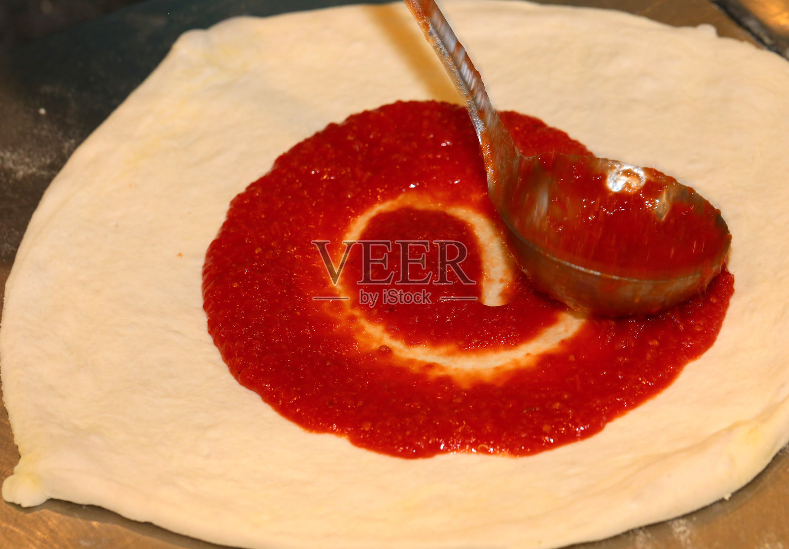 传统意大利披萨面团和用金属勺均匀涂抹的番茄酱照片摄影图片