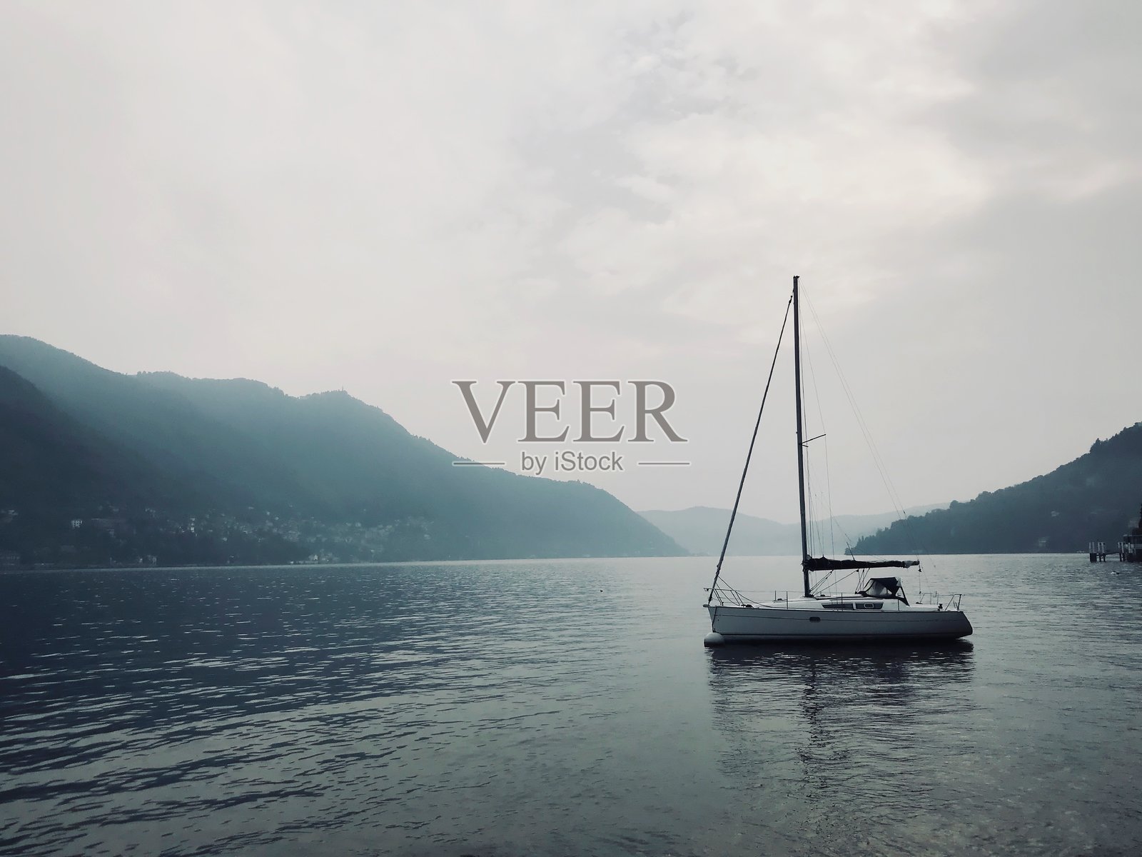 清晨雾气中的科莫湖平静水面上的帆船照片摄影图片