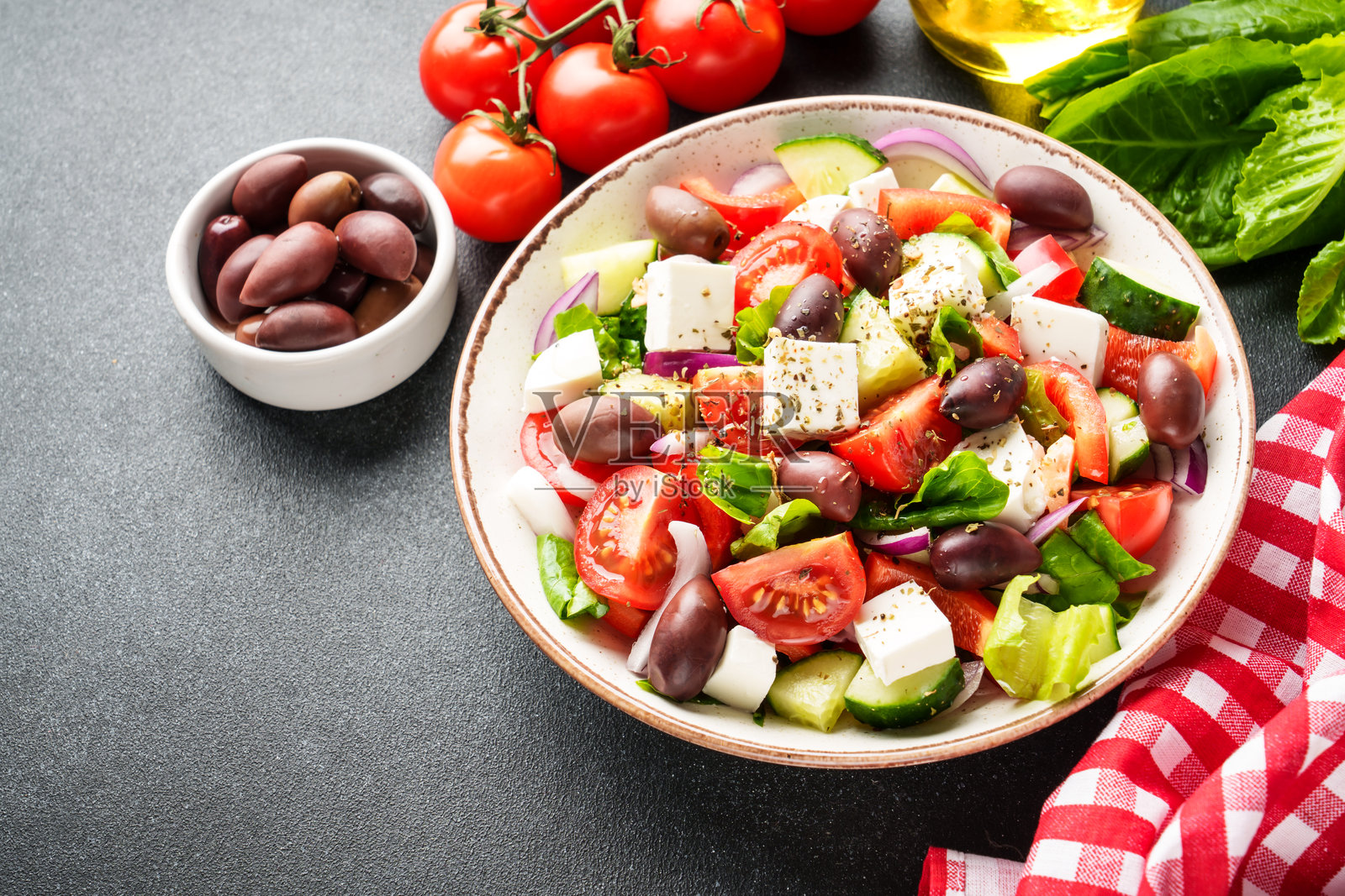 黑色厨房桌子上的手工盘子里的希腊沙拉。照片摄影图片