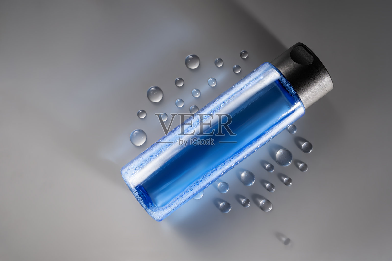 蓝色瓶装护肤爽肤水，灰色背景上的水滴，极简美妆产品展示照片摄影图片