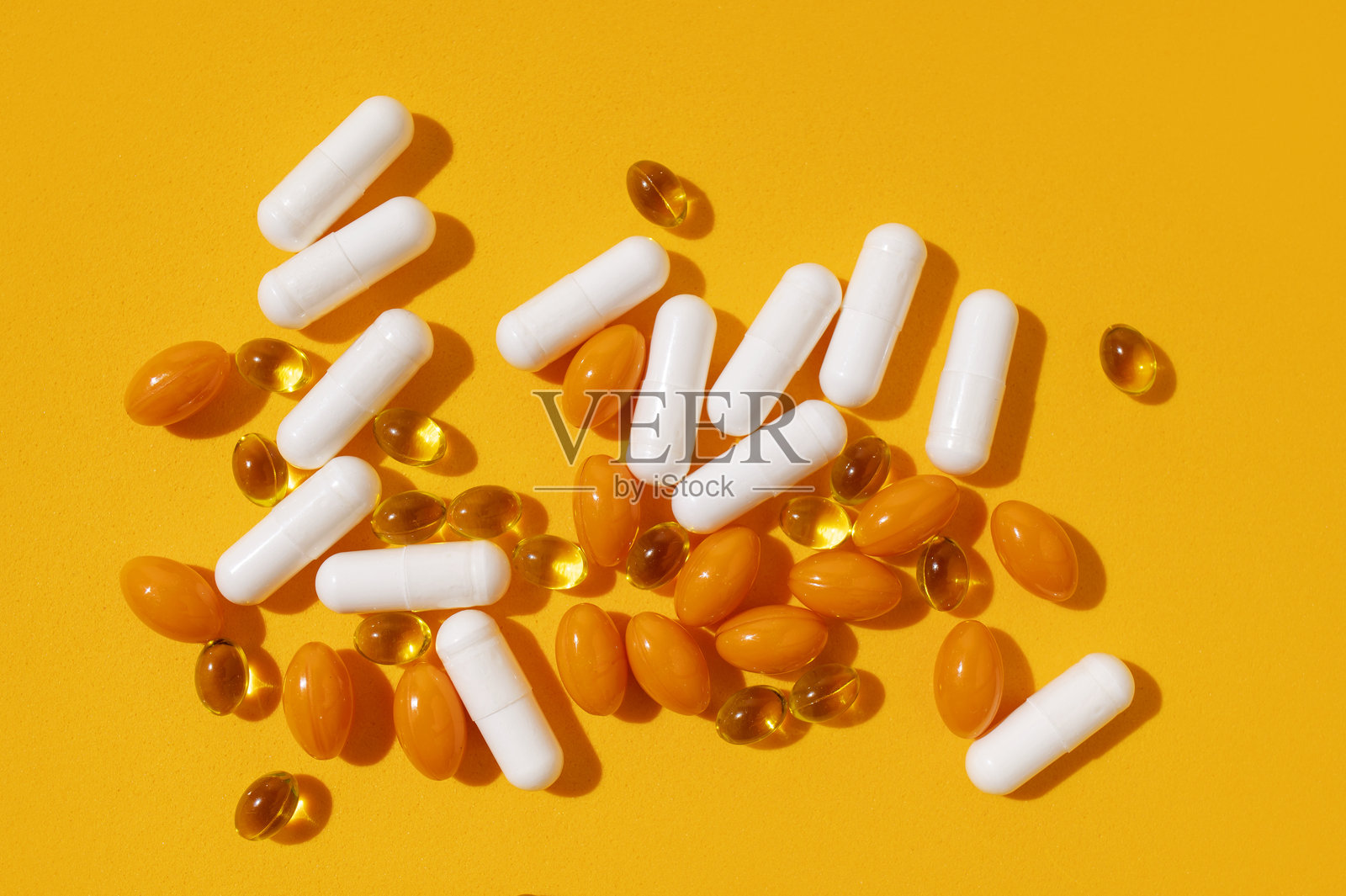 不同种类的维生素胶囊、天然补充剂和营养保健品，背景为黄色，俯视图。药片、药丸特写。医疗药品背景。阳光照明。照片摄影图片