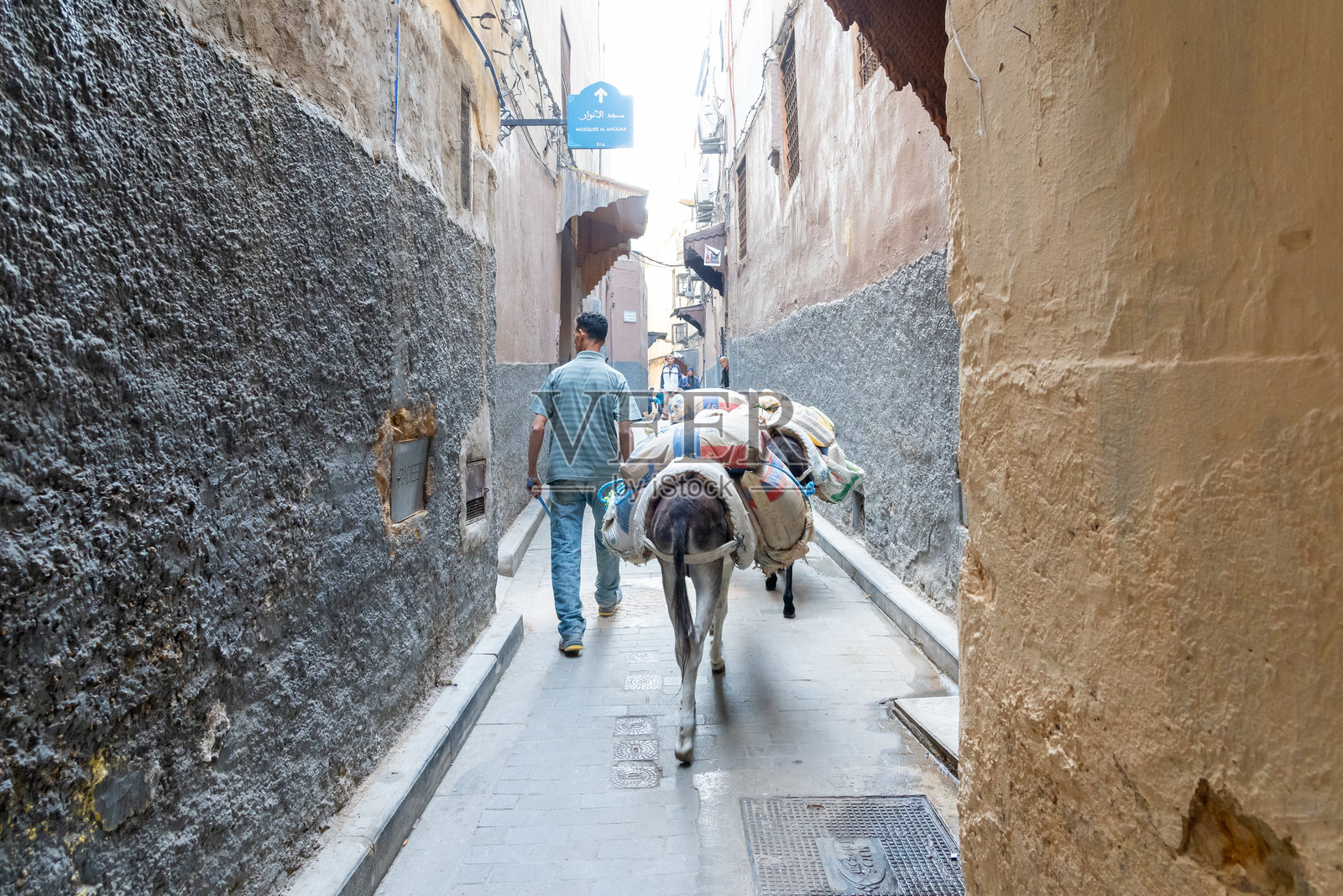 摩洛哥费斯老城狭窄小巷中驴子运输建筑材料。照片摄影图片