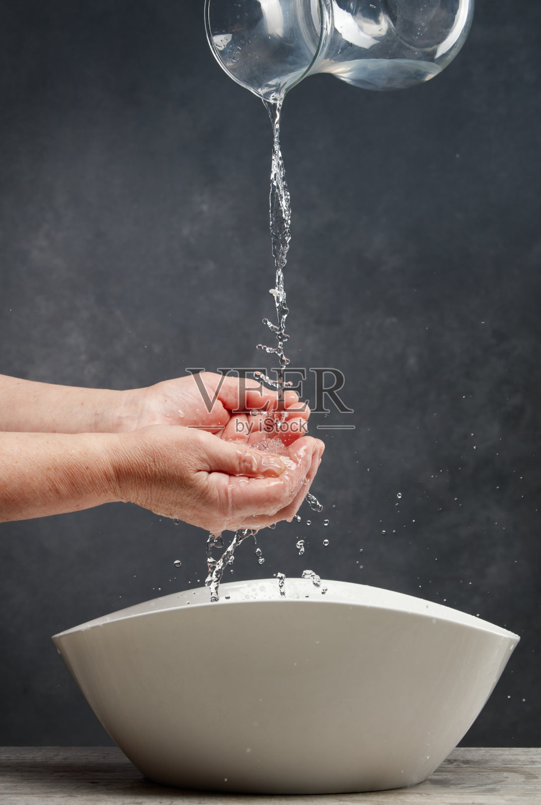 水从玻璃罐中溅出，洒在一位老年女性的手掌上。照片摄影图片