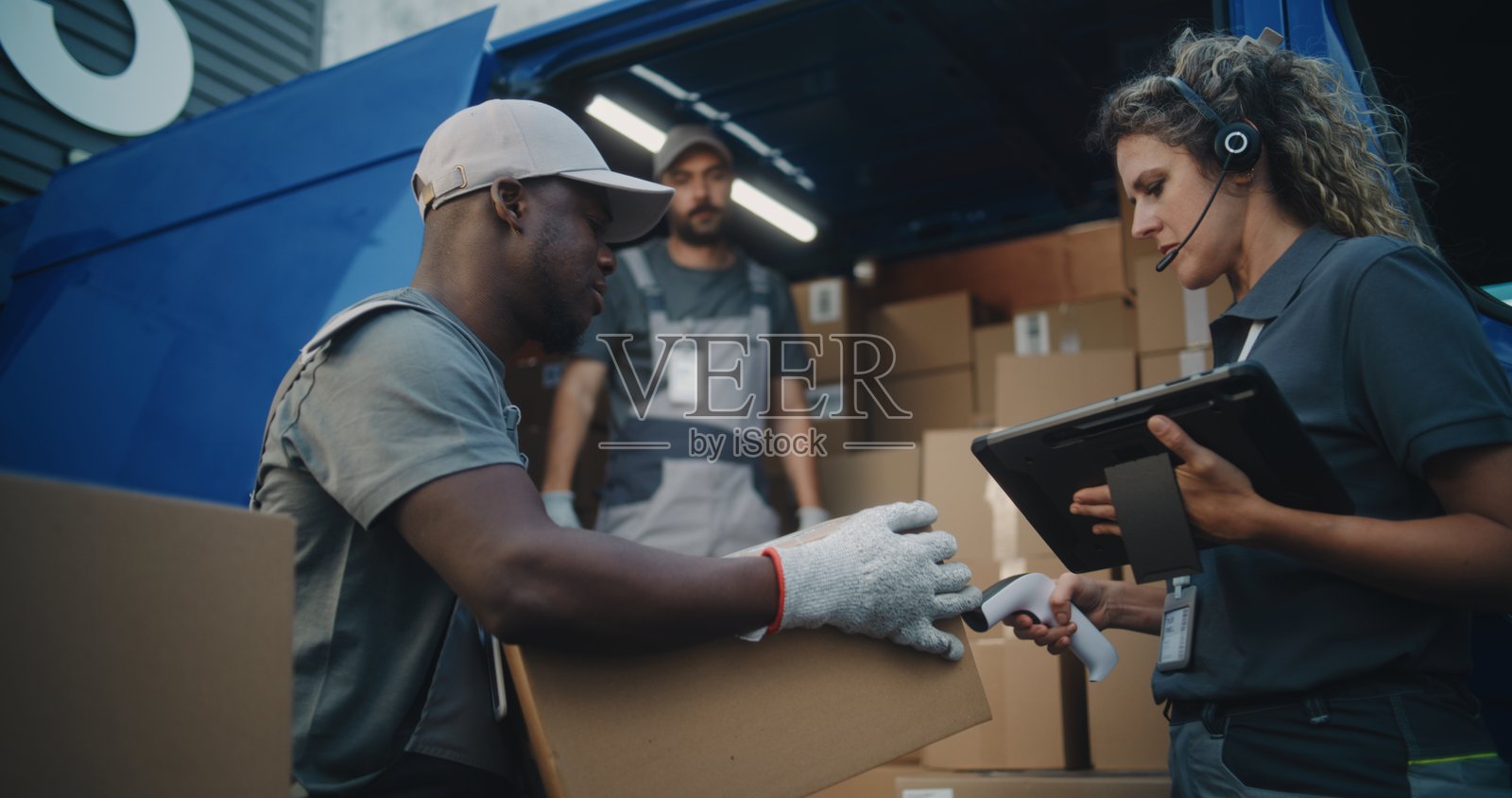 员工们正在装载送货卡车。女经理使用数字平板和条形码扫描器。照片摄影图片