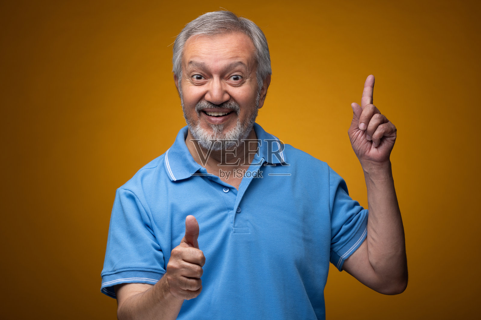 穿着蓝色T恤的老年帅气男性肖像照片，背景为黄色。照片摄影图片