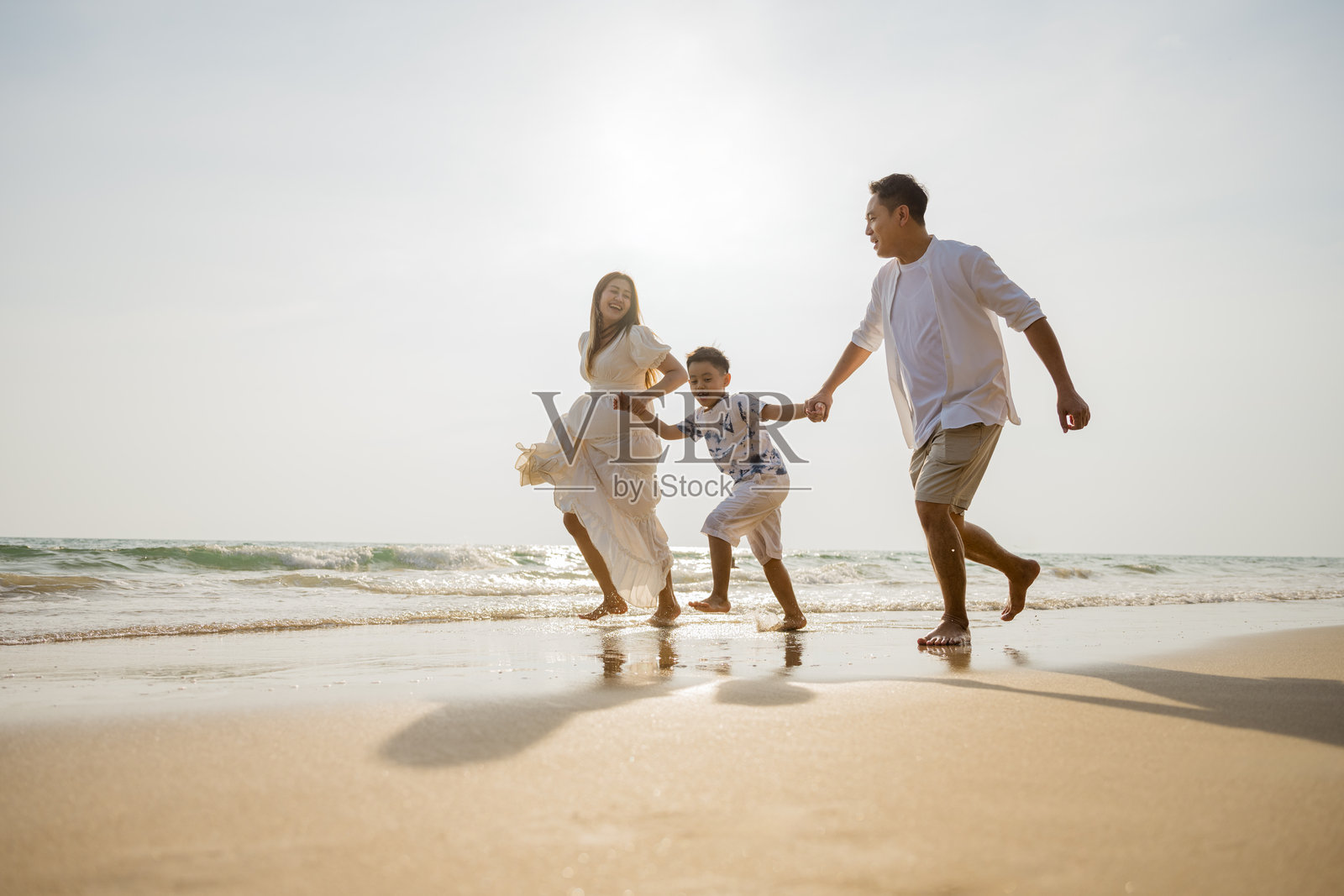 亚洲家庭海滩度假。孩子们和父母一起放松。人们的生活方式。一个三口之家，一名男性和两个孩子正在海洋中玩耍。男性正牵着孩子们的手。照片摄影图片