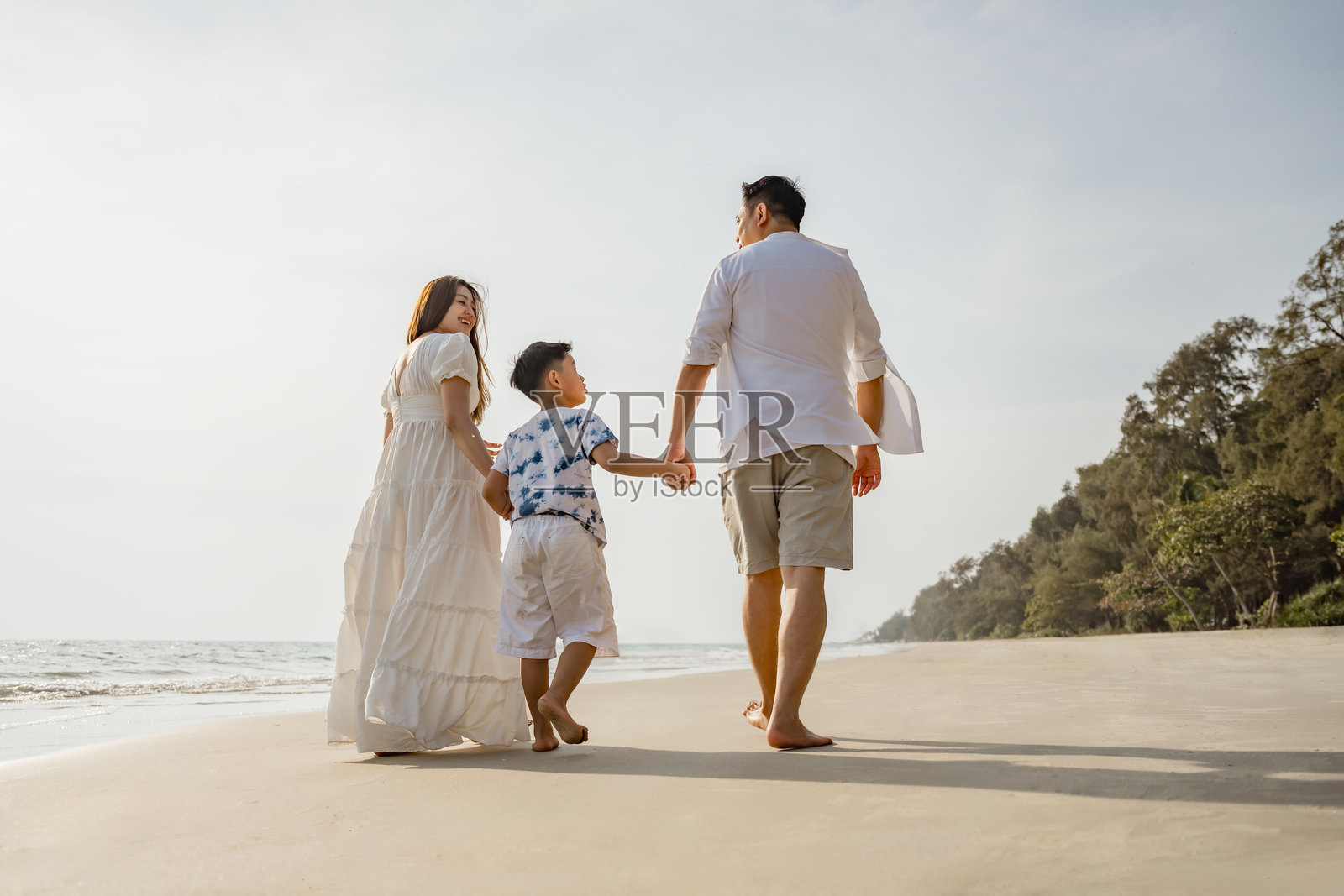 亚洲家庭海滩度假。孩子们和父母一起放松。人们的生活方式。一个三口之家，一名男性和两个孩子，正在海滩上散步。男性牵着两个孩子的手。照片摄影图片