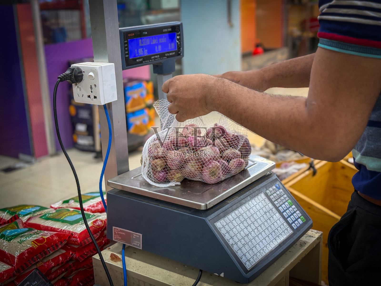 在杂货店中用数字秤称重新鲜红洋葱的手照片摄影图片