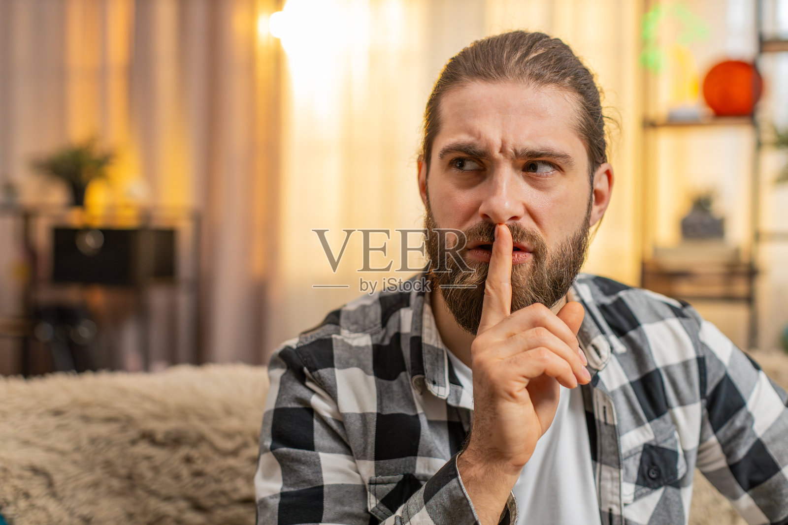 年轻男子在家中用手指放在嘴唇上示意安静，仔细倾听，神情紧张，发出安静的信号照片摄影图片