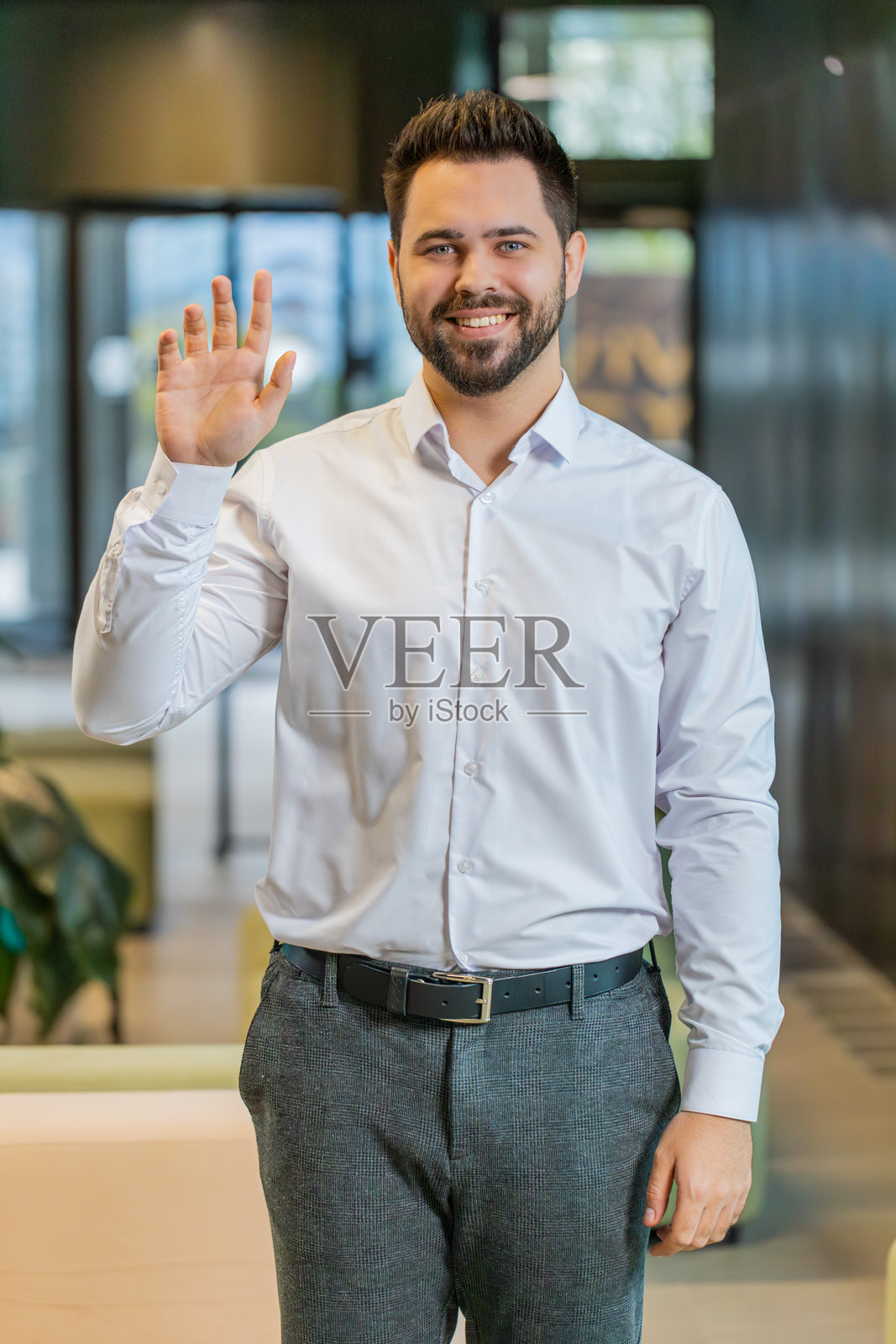 快乐的年轻白人商人在现代办公室大堂里微笑着看向镜头并挥手问好照片摄影图片