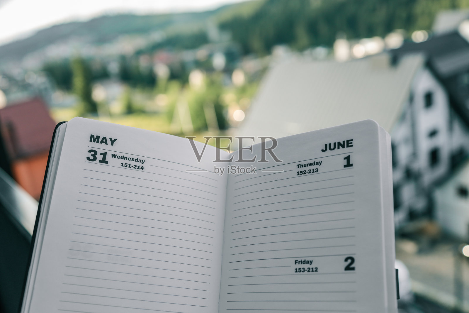 户外展示的打开的计划本，显示5月31日和6月1-2日的页面，背景为模糊的城市景观和森林山丘。时间管理、规划、生产力、商业和远程工作的概念。照片摄影图片