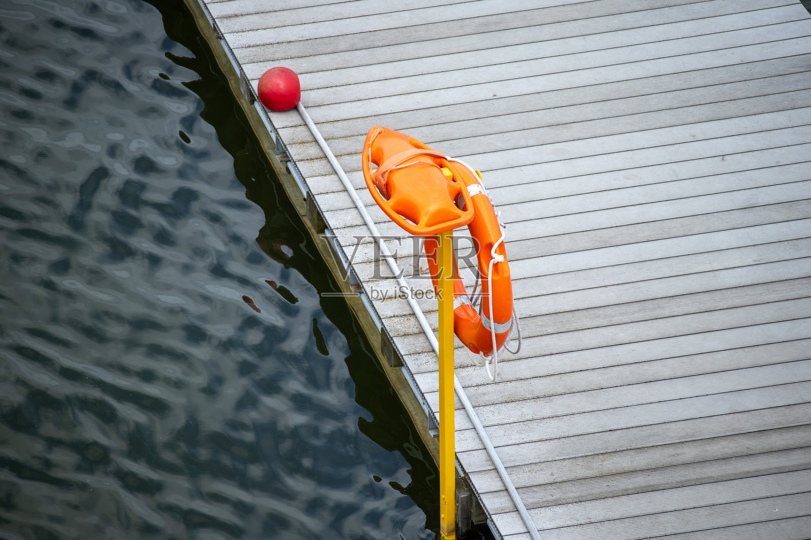 一个橙色的救生圈和救援浮标安装在木栈道旁的黄色杆子上。照片摄影图片