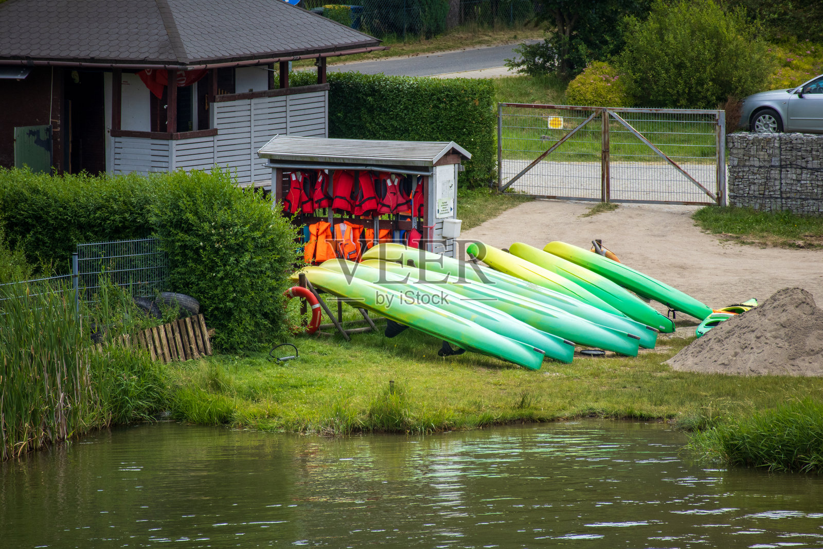 五颜六色的皮划艇和救生衣堆放在宁静湖岸的租赁站附近。照片摄影图片