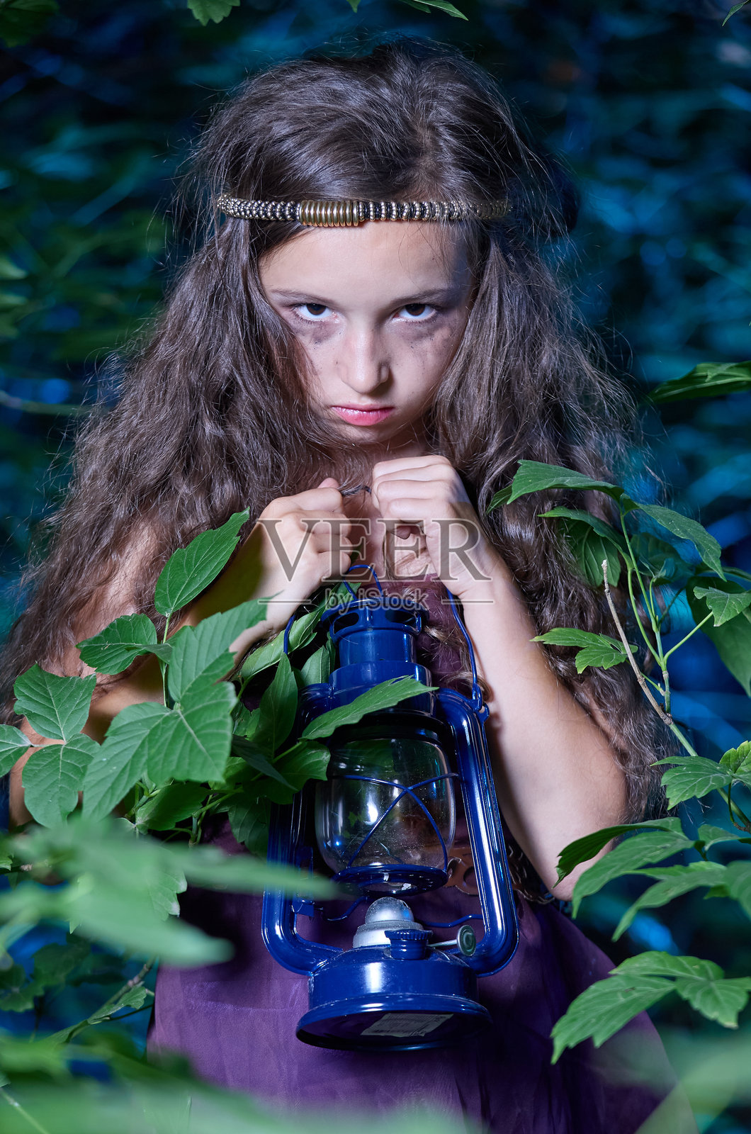 穿着紫色裙子的美丽少女手持煤油灯，忧郁地看着镜头。照片摄影图片