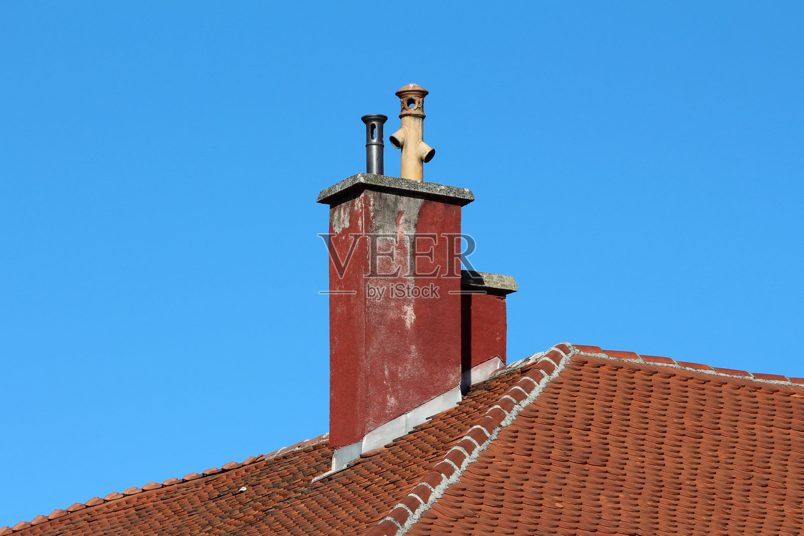 红色烟囱与双烟道，位于蓝天下的陶土瓦屋顶上照片摄影图片