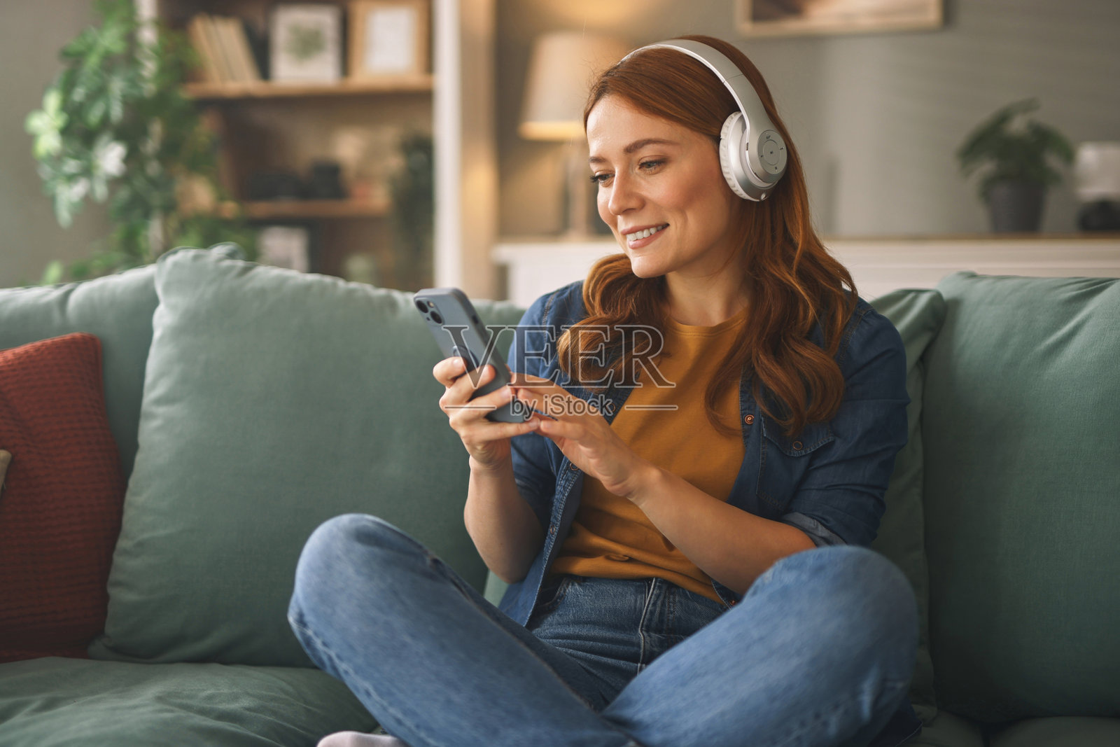 年轻女性在沙发上放松，听音乐并使用智能手机照片摄影图片