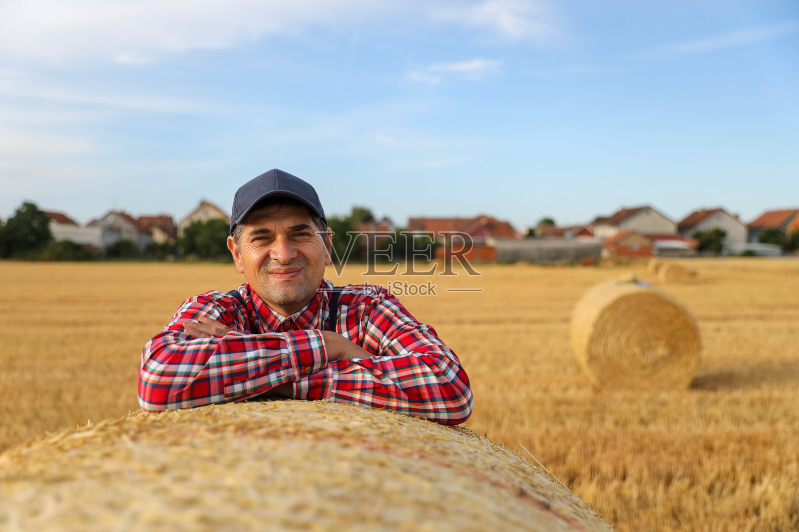 自信的农民靠在收割后的干草堆上照片摄影图片