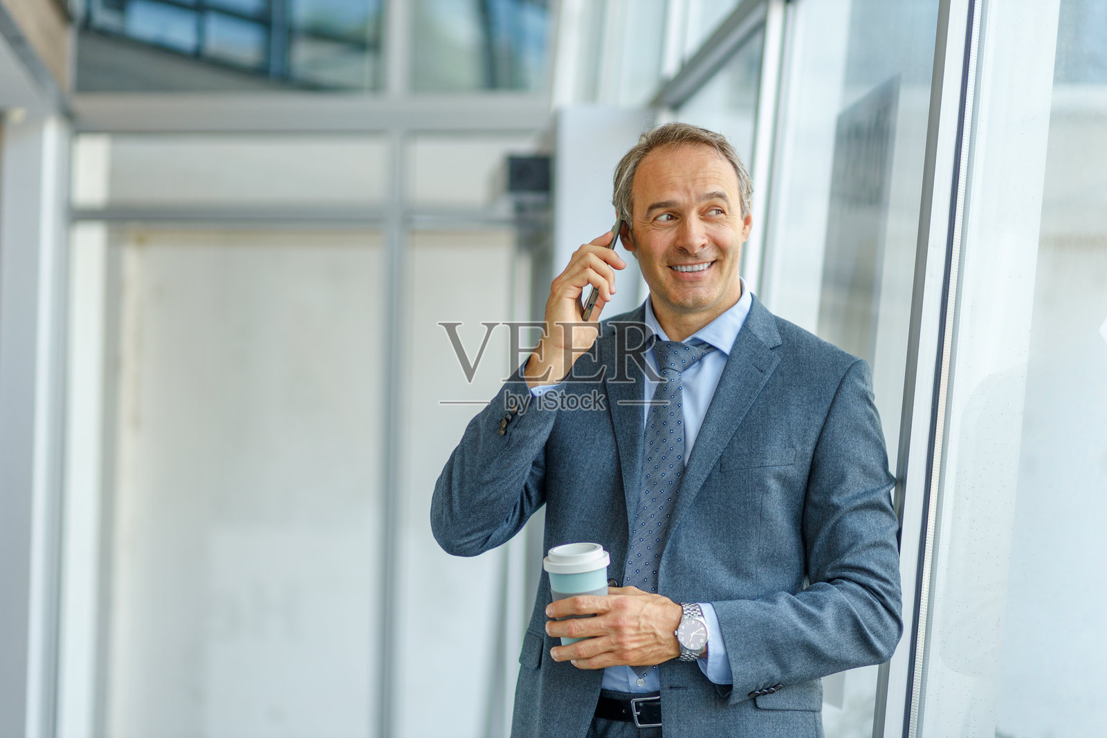 微笑的商人在现代办公室里一边打电话一边喝咖啡照片摄影图片