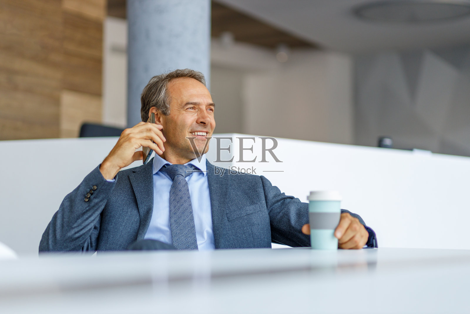 商人在办公室里一边打电话一边拿着咖啡杯照片摄影图片