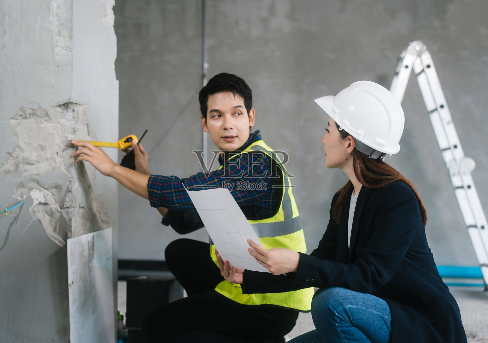 亚洲男女工程师穿着安全背心和头盔，在现场检查结构元素，审查蓝图，规划材料选择，包括砖、钢和混凝土，进行家庭装修项目。照片摄影图片