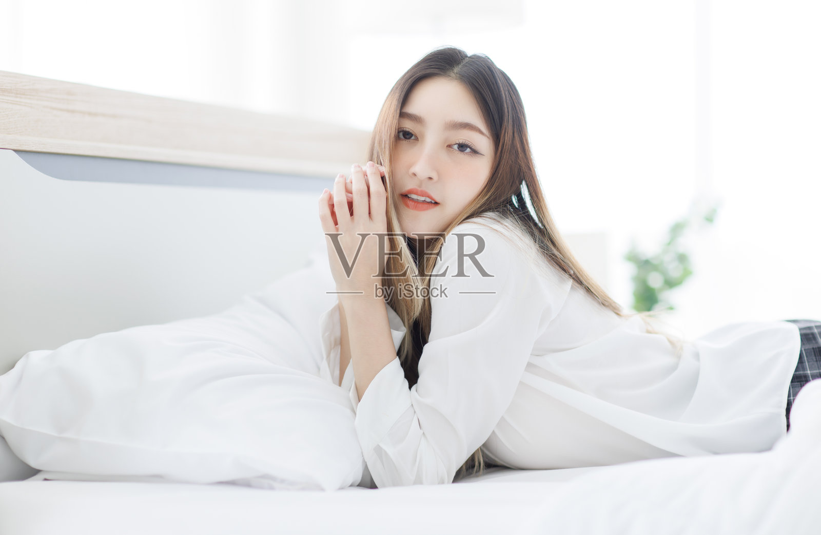 亚洲年轻快乐迷人的美丽女性在阳光下放松，享受宁静的时刻，微笑着躺在明亮的白色卧室舒适的床上，度过周末早晨，感受生活的舒适与健康。照片摄影图片