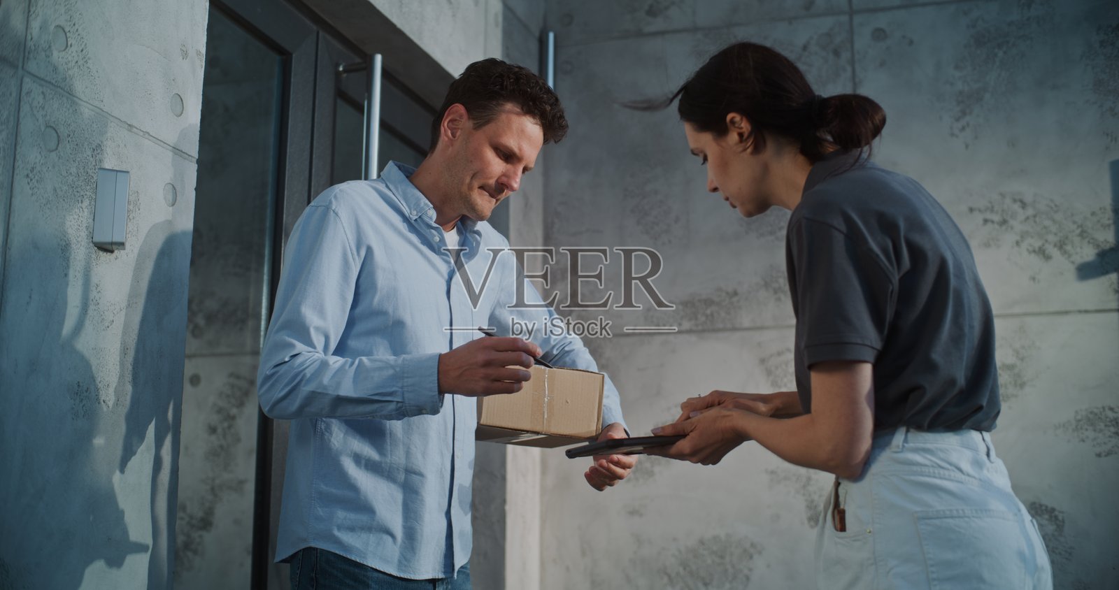 女邮递员将包裹递送给收件人，正在数字平板上获取客户签名照片摄影图片