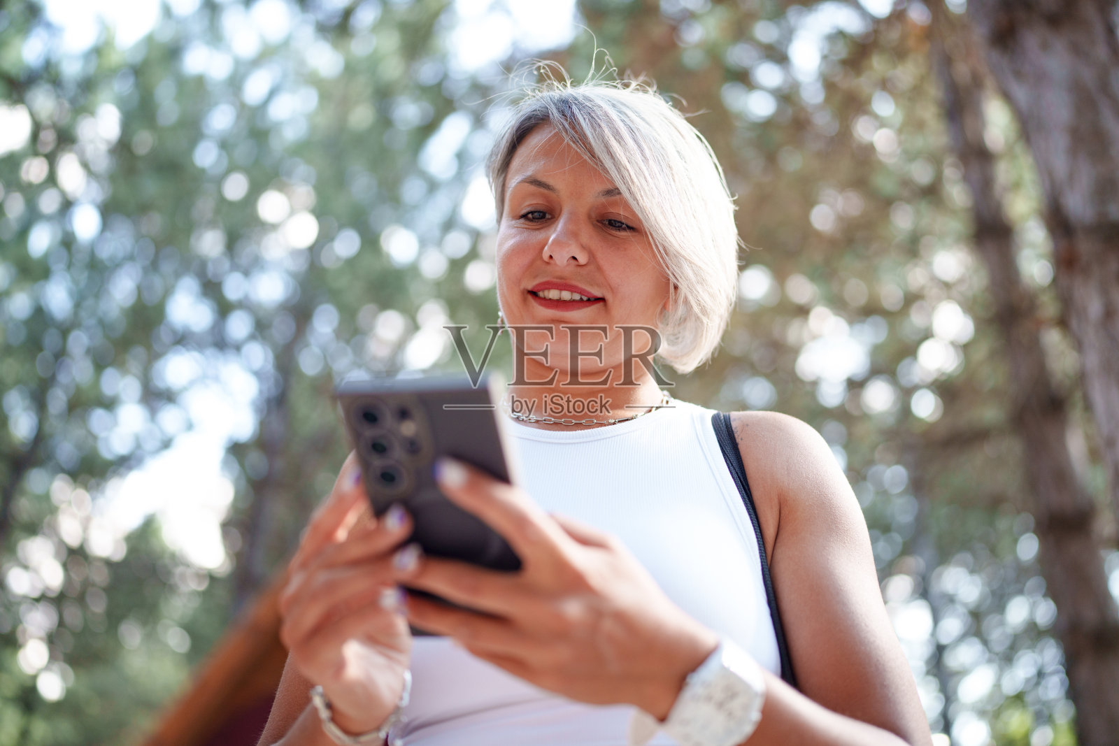 在树木繁茂的公园里使用手机的女性照片摄影图片