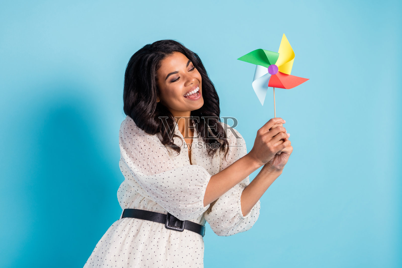 年轻可爱快乐兴奋的时尚非洲女孩在蓝色背景下玩风车照片摄影图片