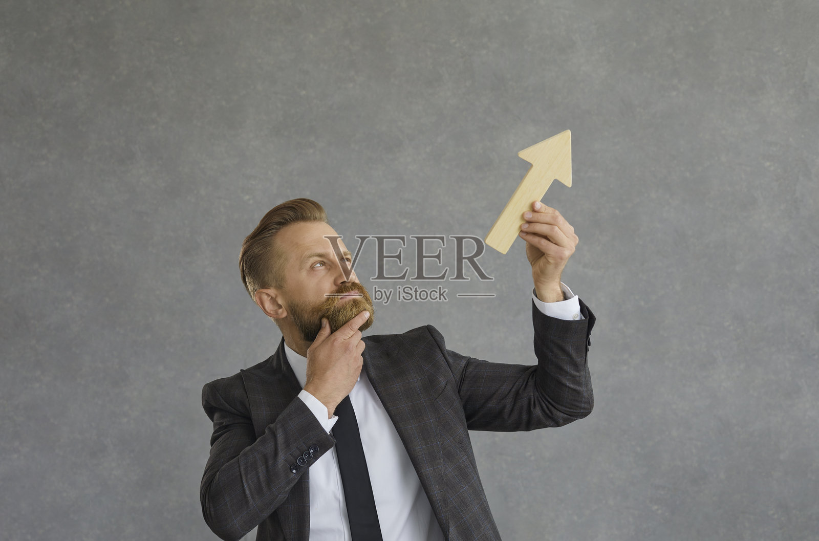 商人手持向上的箭头，思考着业务增长并感到怀疑照片摄影图片