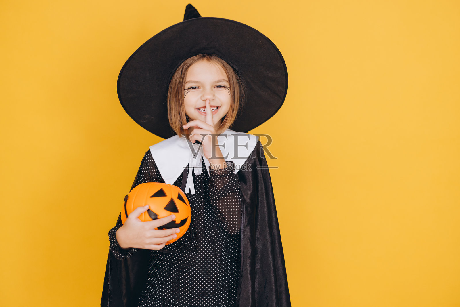 小女巫抱着南瓜在黄色背景下保守秘密照片摄影图片