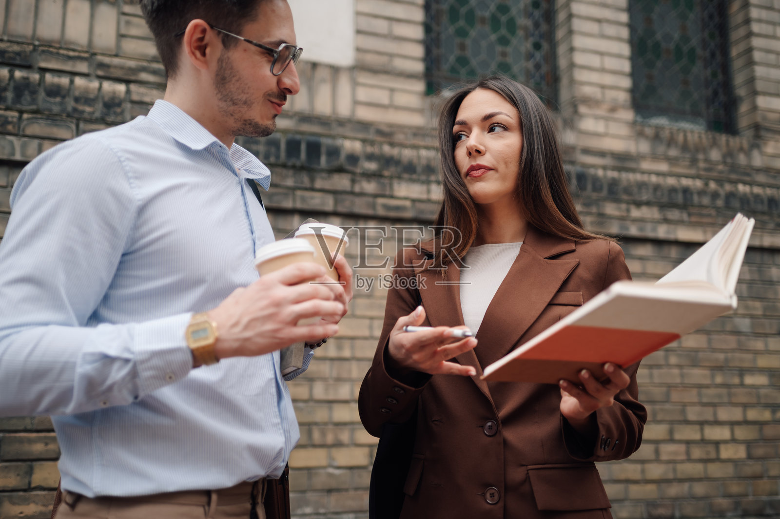 商务同事一边喝咖啡一边讨论工作，手中还拿着书籍照片摄影图片