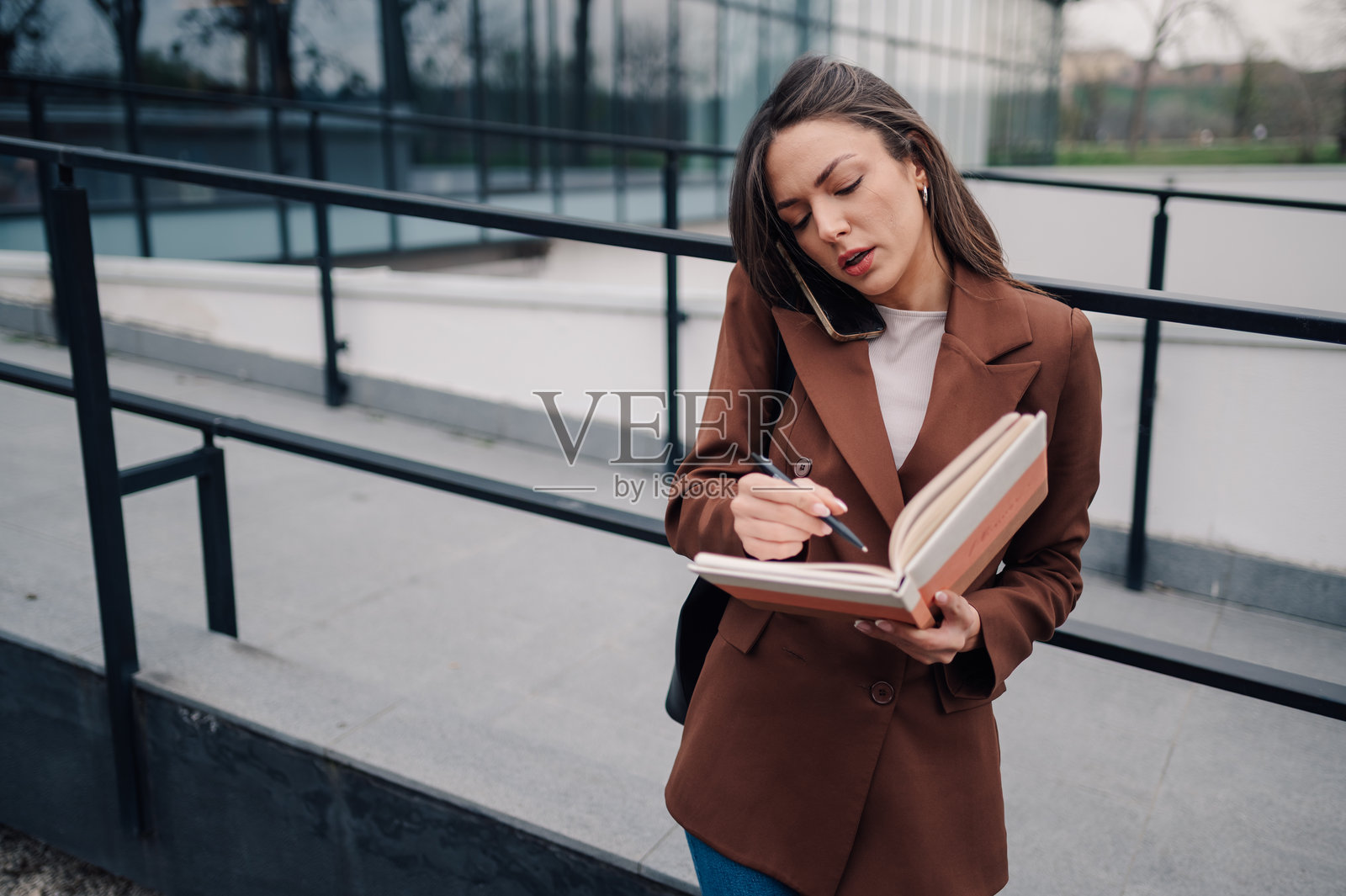 女商人在办公室外一边打电话一边做笔记照片摄影图片
