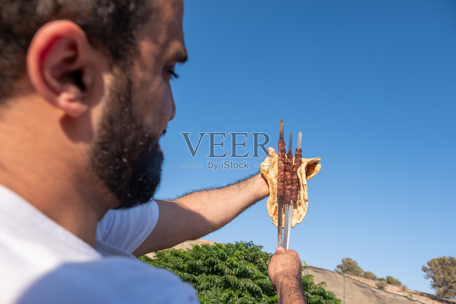 男子在晴朗的蓝天下享受烤肉串和扁面包照片摄影图片