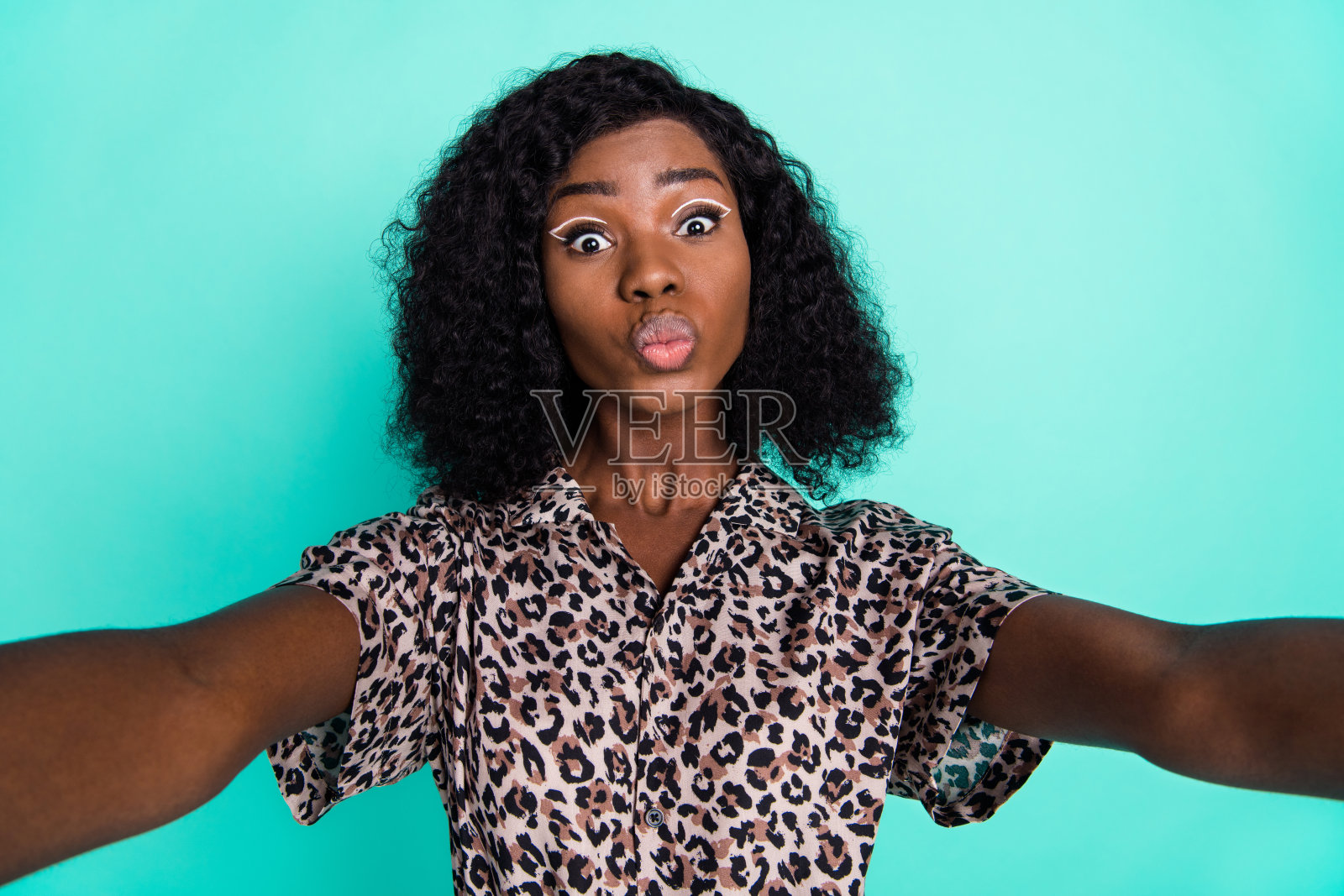 浪漫女士自拍送空气吻，穿着豹纹衬衫，背景为青绿色。照片摄影图片