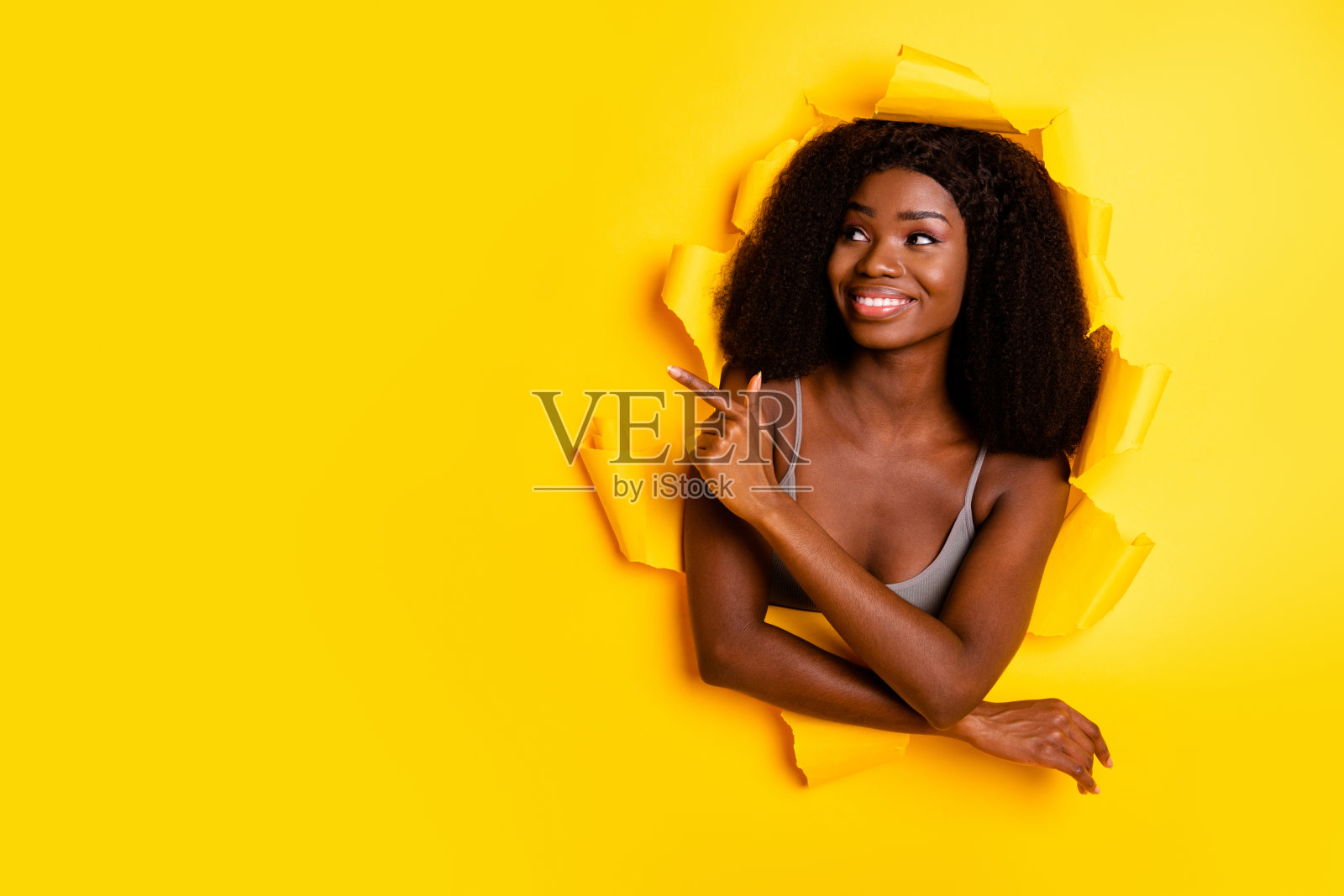 吸引人的快乐女孩撕破纸板，展示推荐的空白广告空间，背景为明亮的黄色。照片摄影图片