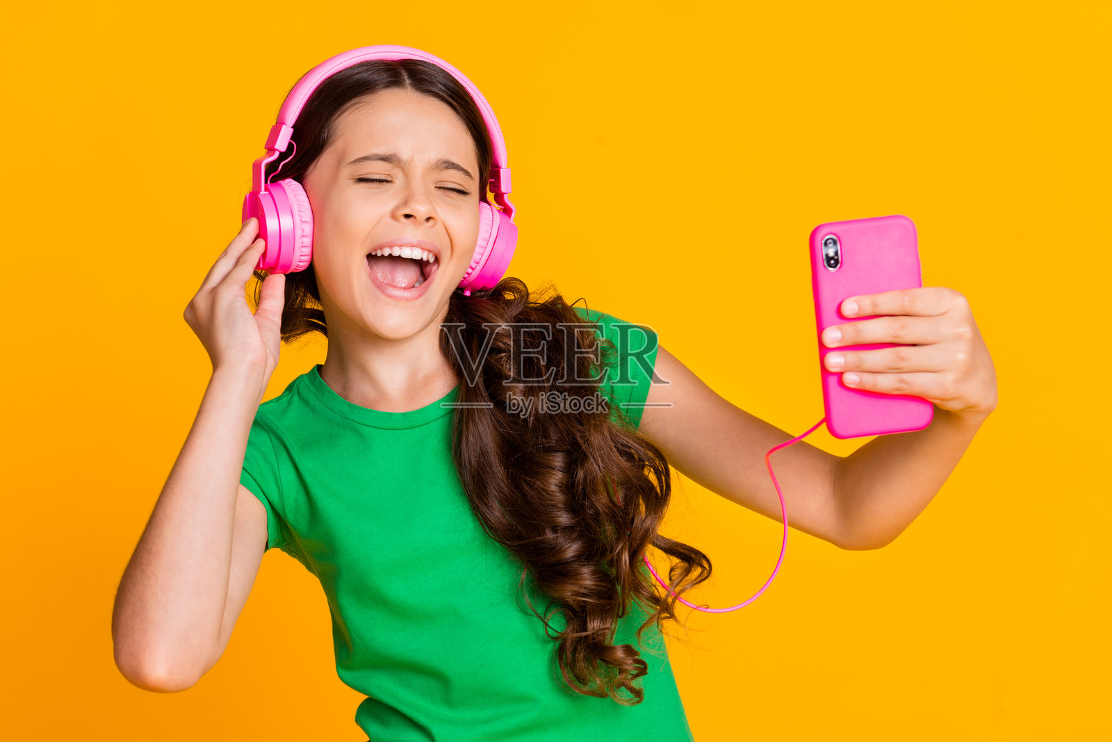 年轻快乐兴奋的时尚女孩在黄色背景下享受音乐，戴着耳机。照片摄影图片