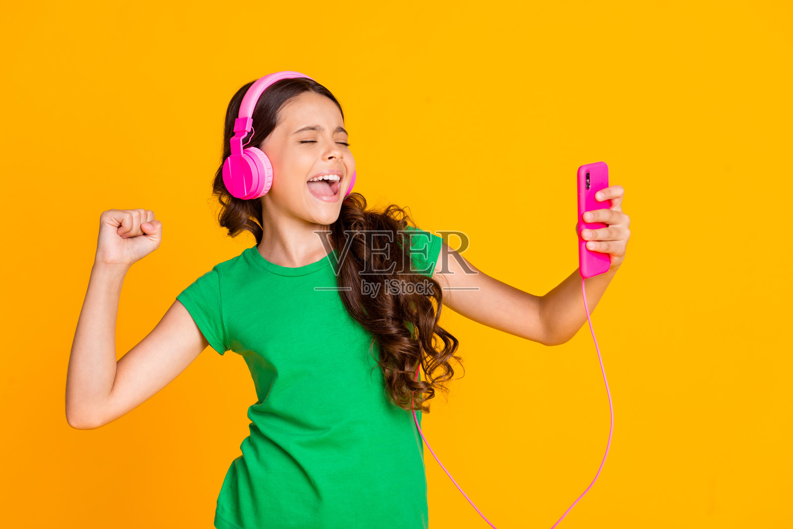 快乐兴奋的可爱女孩在黄色背景下享受听音乐的时光，面带微笑。照片摄影图片
