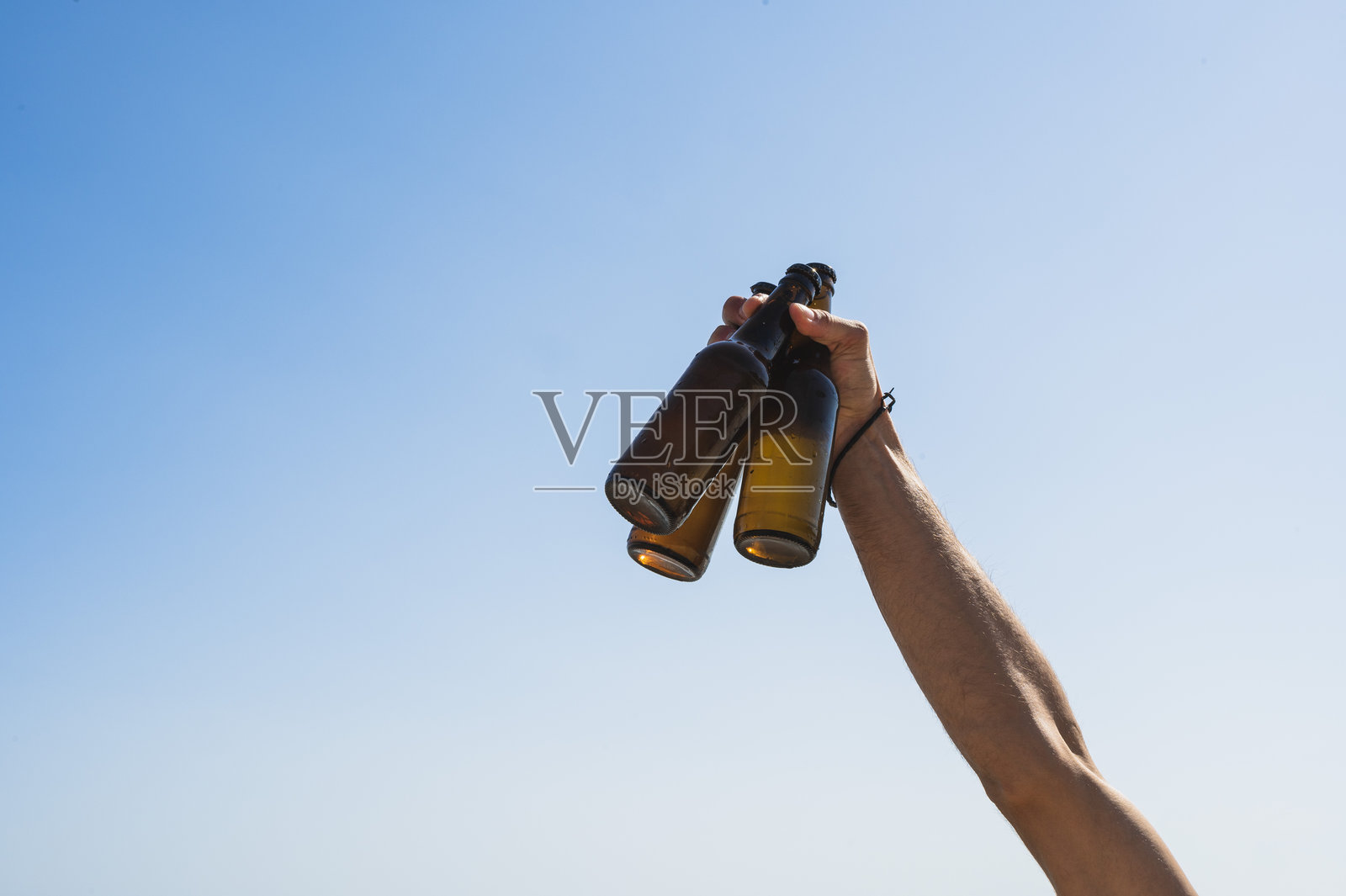 男人在蓝天背景下高举三瓶啤酒照片摄影图片