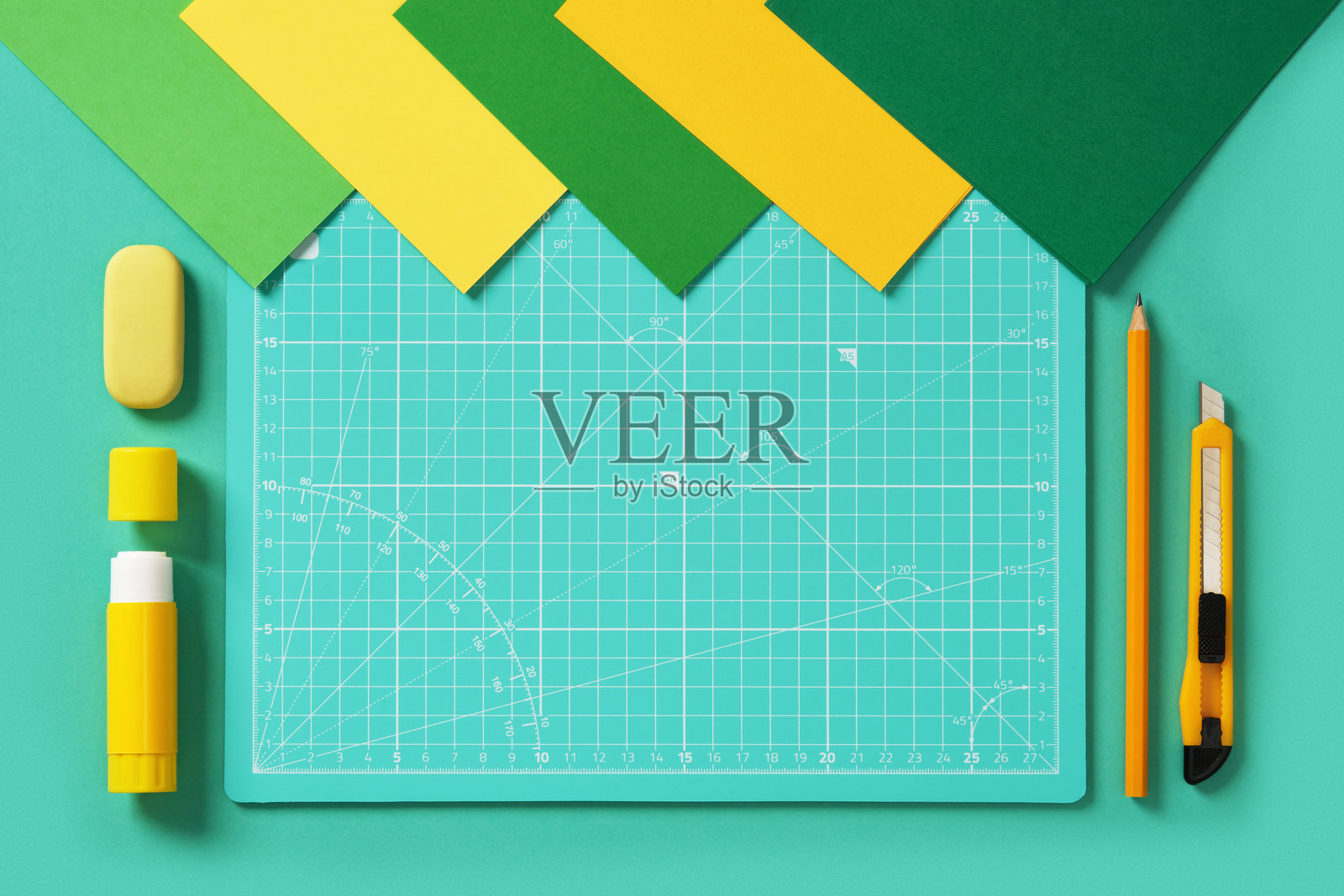 从上方俯视一个绿色和黄色的手工桌。手工刀、铅笔、橡皮、胶水、切割垫和彩色纸。留有空间供您填写文本。照片摄影图片