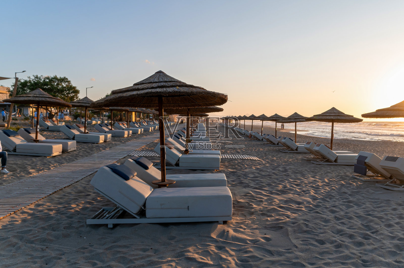 克里特岛希腊日落时分的放松海滩景观，躺椅和伞整齐排列。照片摄影图片
