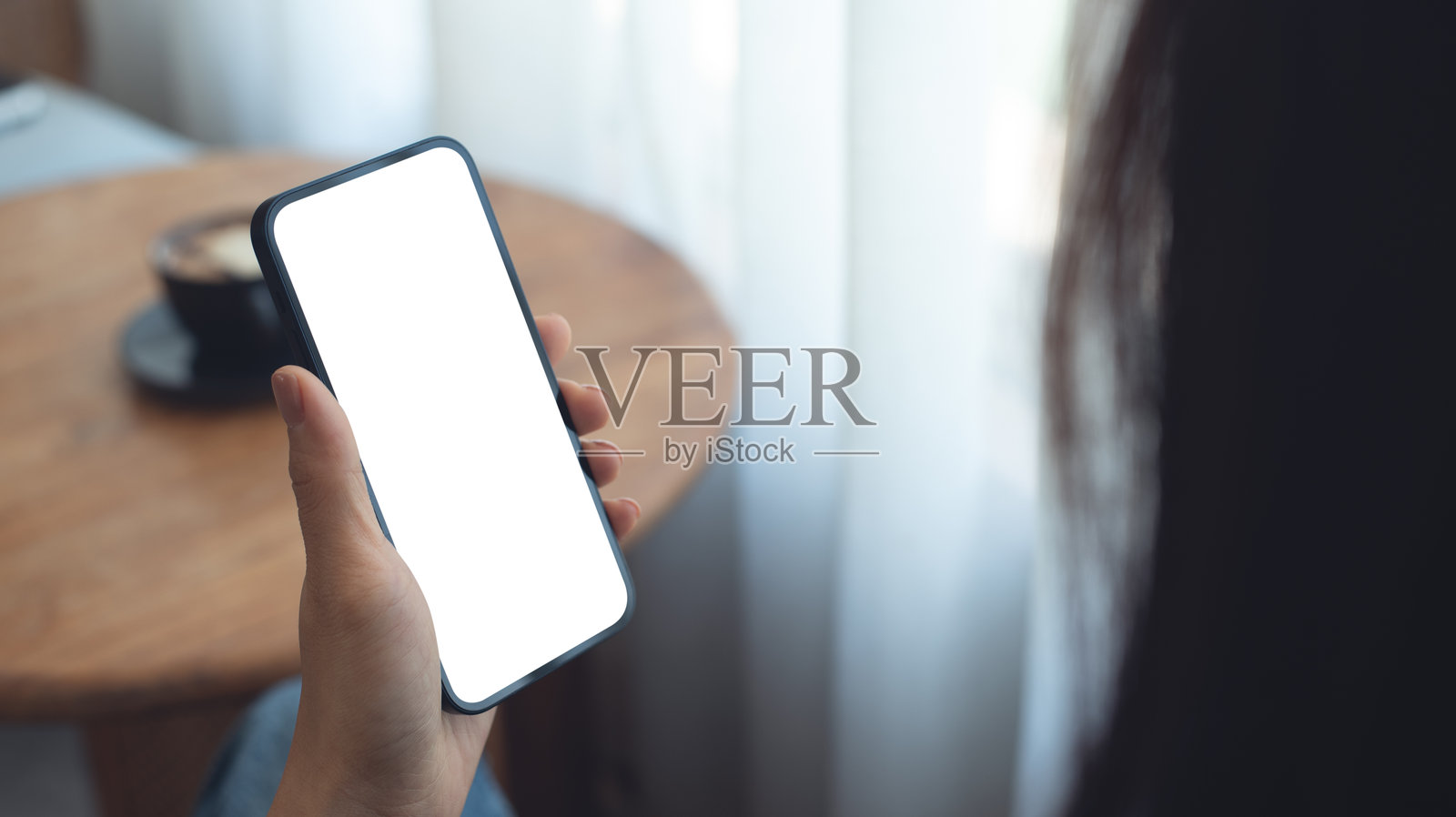 空白屏幕手机的模型。女性手持手机，在咖啡店使用，白色空白区域可用于网页模板。社交媒体营销，移动应用设计，科技设备，特写镜头。照片摄影图片