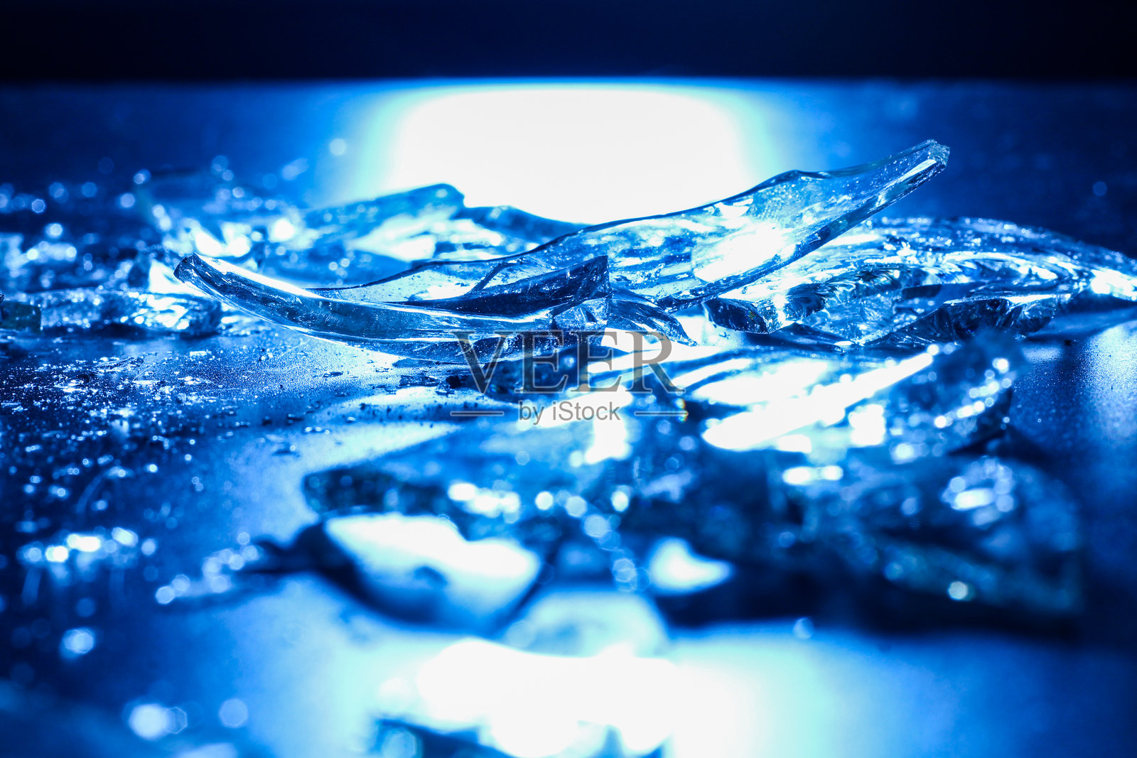 黑暗表面上的破碎玻璃碎片，冷蓝色灯光照射照片摄影图片