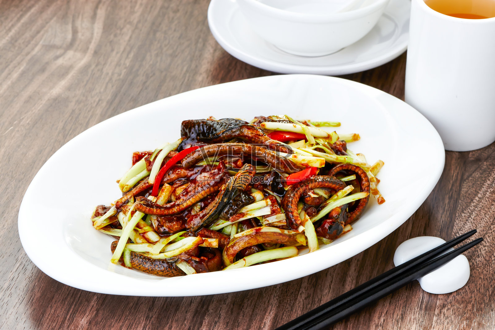 美味的炸鳗鱼配韭菜和辣椒，用筷子盛在盘子里，侧面展示正宗亚洲菜肴。照片摄影图片