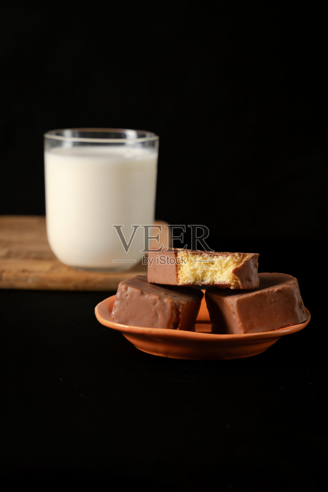 切片巧克力覆盖海绵蛋糕的特写，放在木板上，旁边是一杯牛奶照片摄影图片