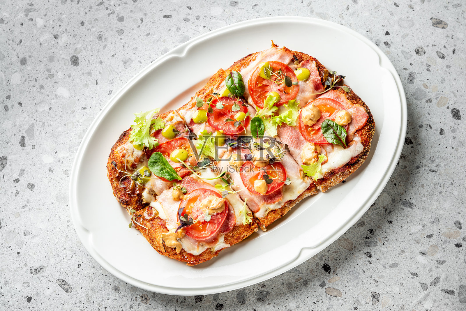 矩形美食披萨，上面放有新鲜的番茄片、奶酪、绿叶蔬菜和香草，摆放在白色盘子上，背景为纹理灰色，俯视图。照片摄影图片