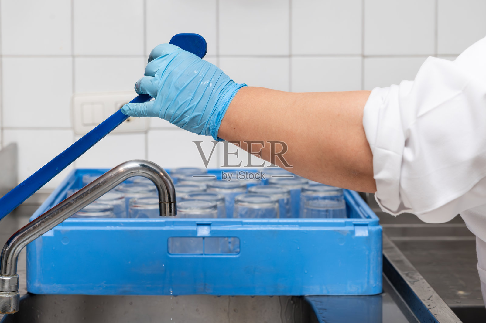 女性戴着乳胶手套的手在商业厨房中进行清洗的特写。照片摄影图片