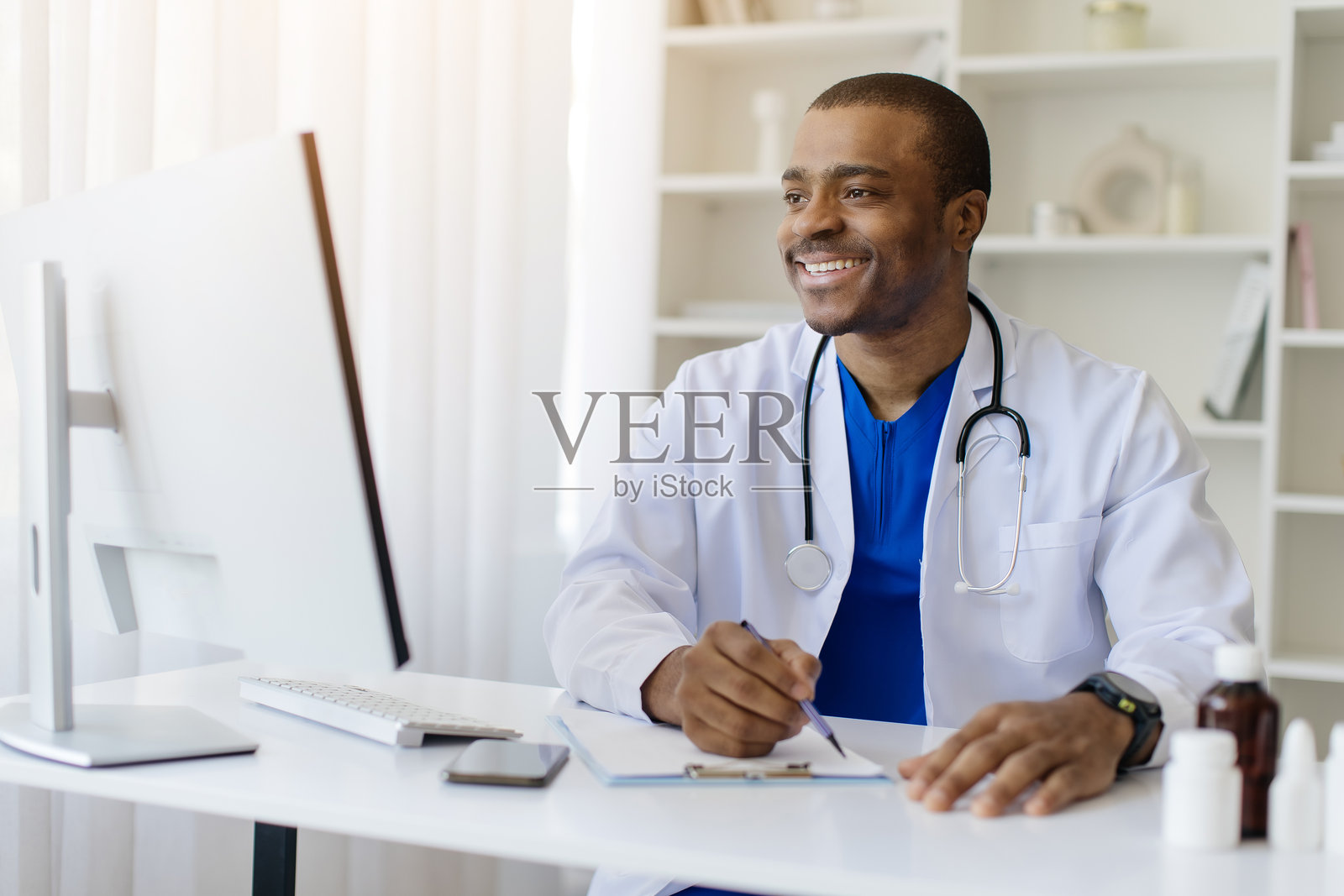微笑的黑人男性医生坐在诊所的桌子前写笔记照片摄影图片