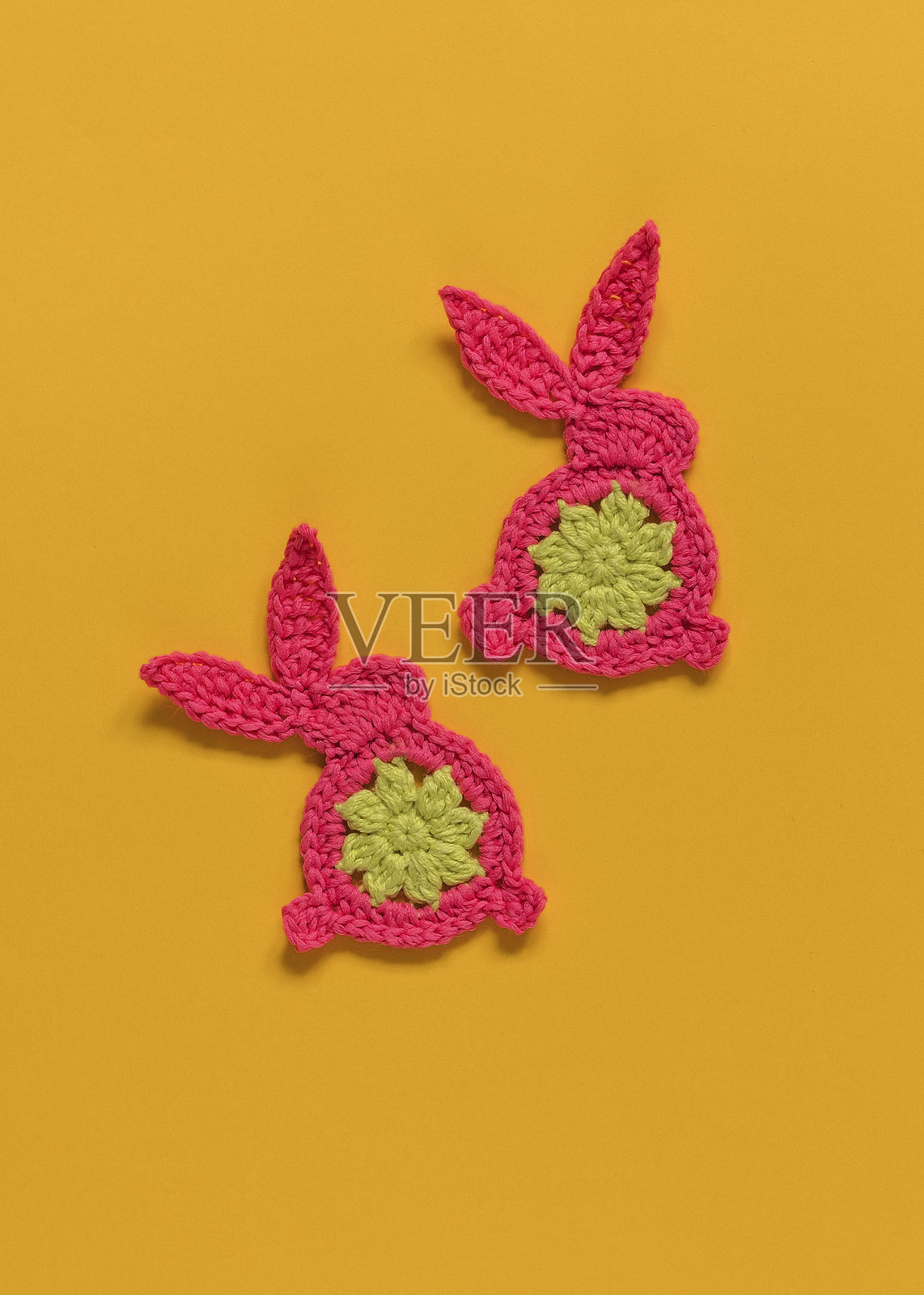 两个粉色和黄色的钩针兔子在黄色背景上。快乐的复活节概念。俯视图。留白空间。照片摄影图片